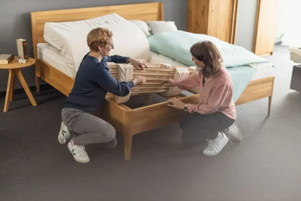 Eine Schlafberaterin der Schlafwerkstatt zeigt einer Kundin das Federelement eines Hüsler Nest Schlafsystems.