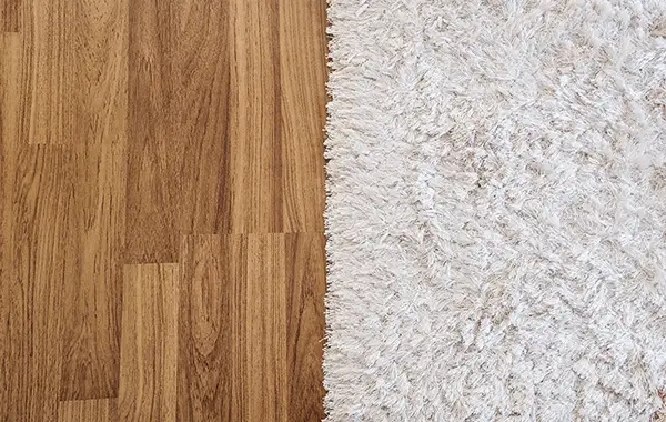 Links ist ein Holzboden zu sehen, rechts ein weicher, weißer Teppich.
