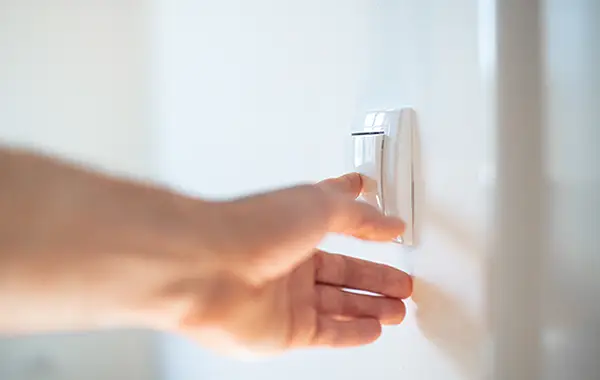 Eine Hand berührt einen Lichtschalter, im Zimmer ist ein angenehmes helles Licht. 