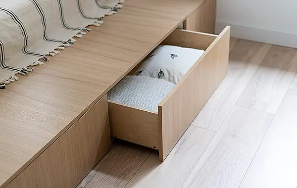 Einbauschubladen aus Holz unter einem Bett. Die Schublade ist geöffnet, darin liegen Kissen.