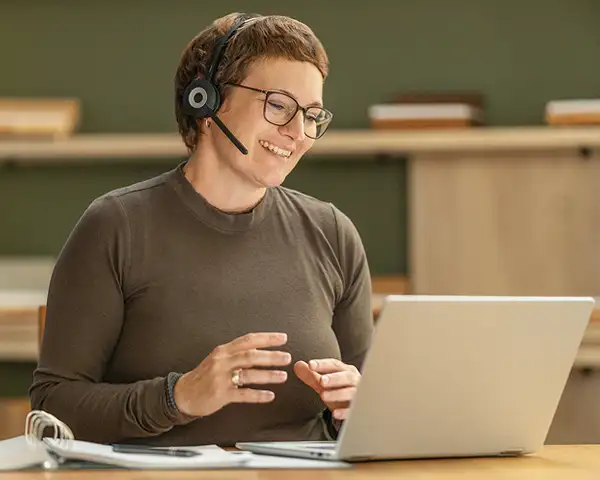 Eine Schlafberaterin (Kathrin Rumpfinger) sitzt mit einem Headset am Laptop in einer Videokonferenz. Sie lächelt freundlich und erklärt etwas.